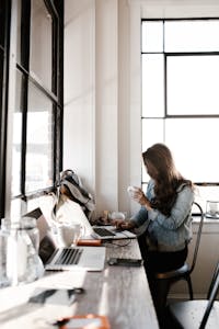 Working with a Crochet Tech Editor. A young woman working on her laptop, sipping coffee in a bright café setting.