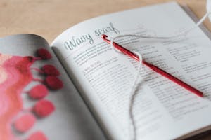 How to write brilliant crochet patterns. Close-up of a yarn and crochet needle on an open craft book, showcasing cozy DIY knitting.