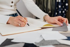 Designing Crochet Patterns. Close-up of hands sketching in a notebook, selecting fabric samples for design.