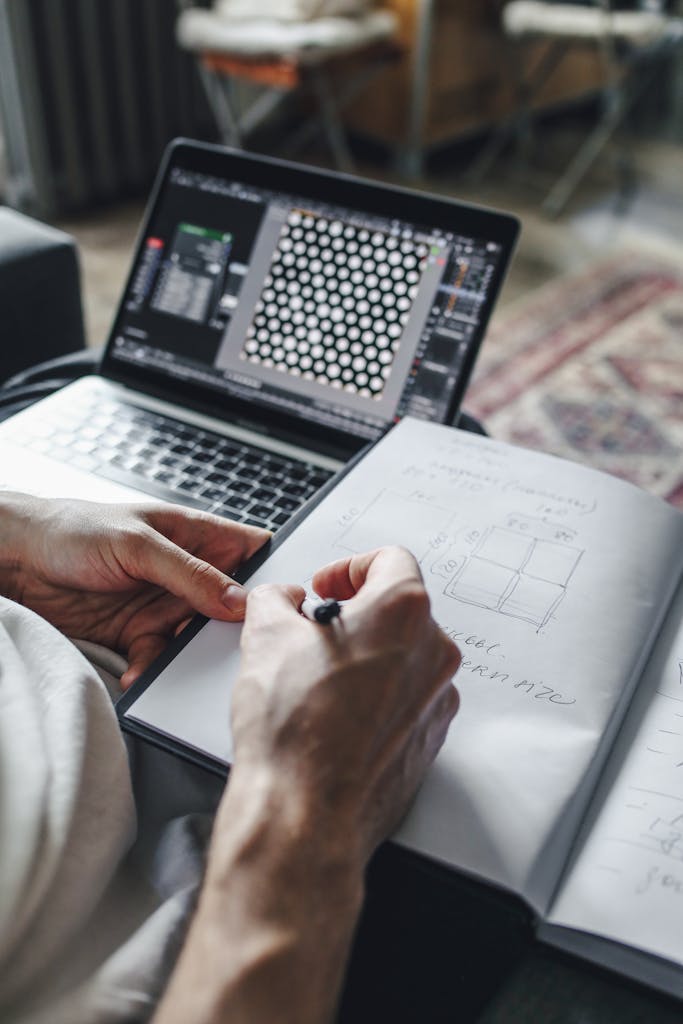 crochet tech editor. Close-up of hands writing in notebook with laptop open on couch, ideal for workspace and productivity themes.