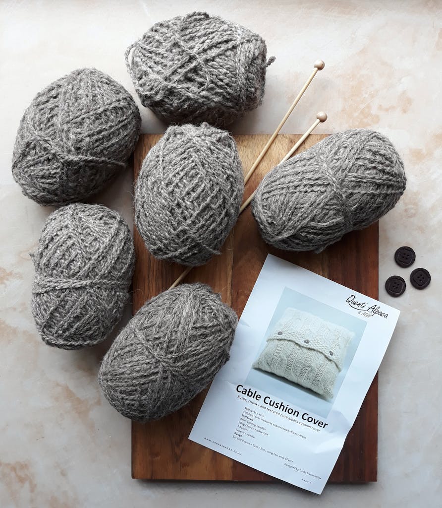 Flat lay of wool yarn, knitting needles, and a cable cushion cover pattern for crafting enthusiasts. Formatting Crochet Patterns example