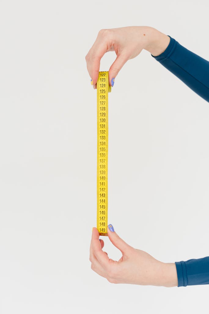 Hands holding a yellow measuring tape on a white background, symbolizing precision.