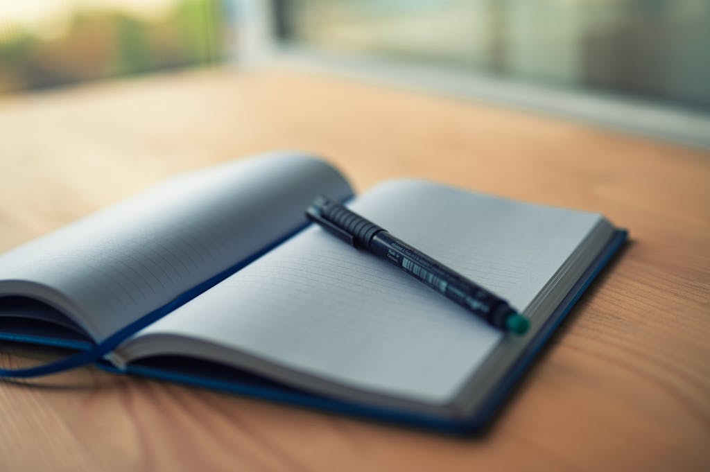 open empty note book on a wooden table with a fineliner pen laid on top. Ready to make notes about how to write effective crochet pattern notes and special instructions.