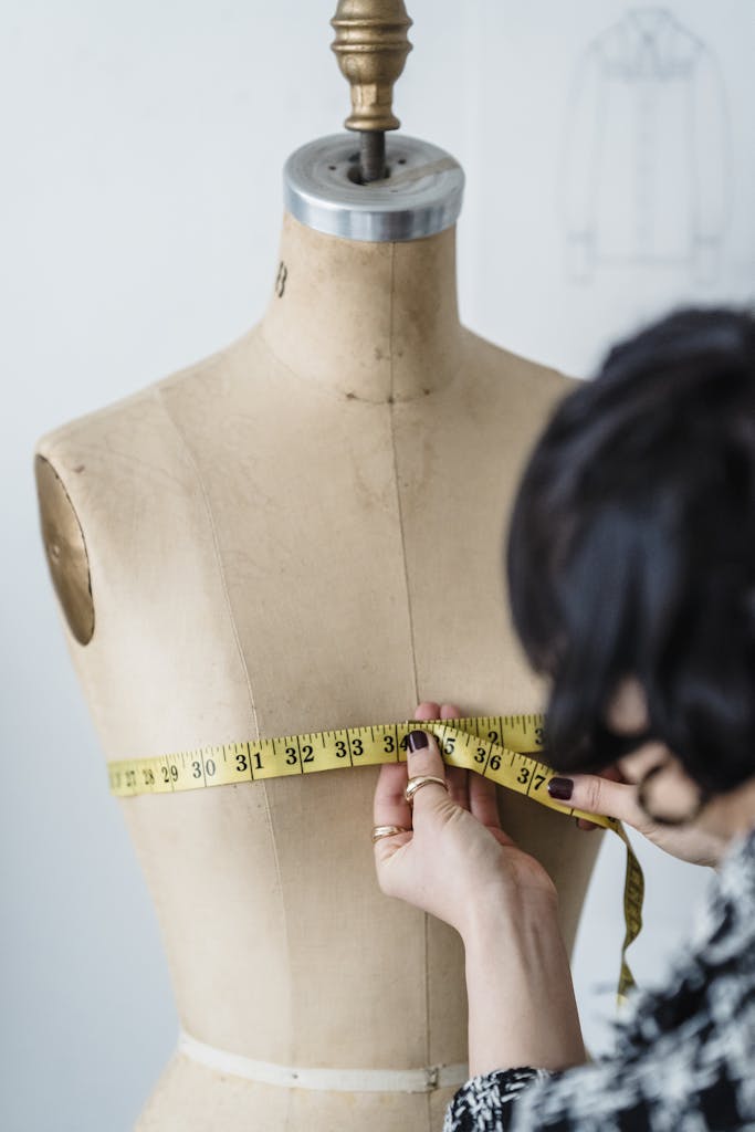 Tailoring expert measuring a mannequin with precision using a tape measure in a studio setting.