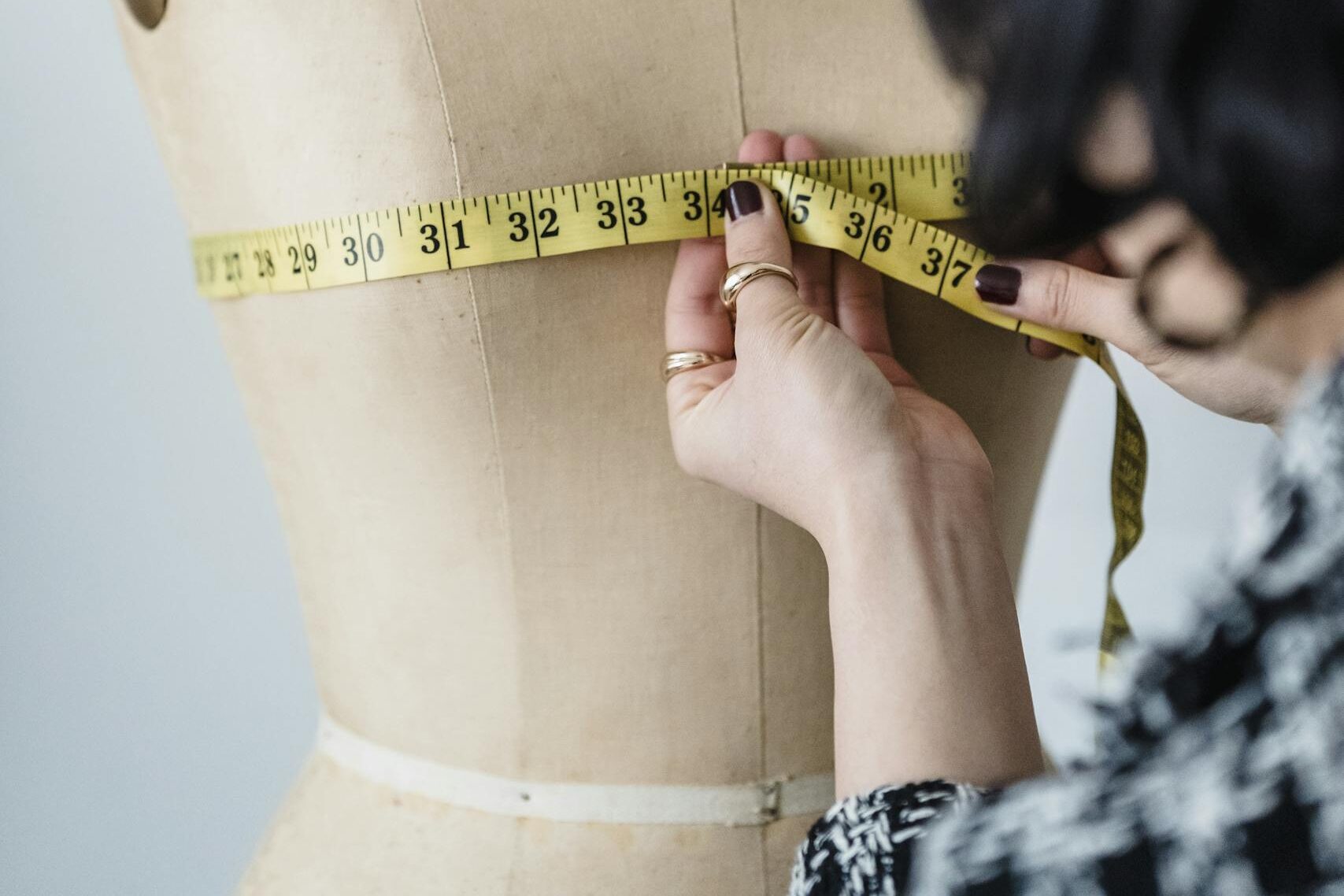 Tailoring expert measuring a mannequin with precision using a tape measure in a studio setting.